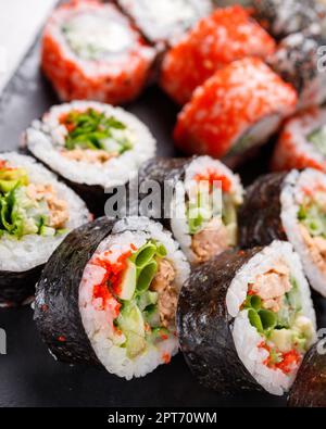 Asiatische Küche. Ein großes Sushi-Set aus verschiedenen Sushi-Rollen wird auf schwarzem quadratischem Metallschiefer serviert. Seitenansicht verschiedener Brötchen mit verschiedenen frischen Zutaten Stockfoto