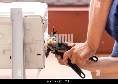 Der Mensch hält einen Schraubenschlüssel in der Hand. Techniker mit Schraubenschlüssel bei der Installation einer modernen Klimaanlage. Arbeiter auf der Straße installiert Außenluftkond Stockfoto