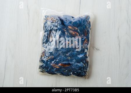 Gekochtes gefrorenes Miesmuscheln Fleisch in Vakuumverpackung auf Holztisch Stockfoto