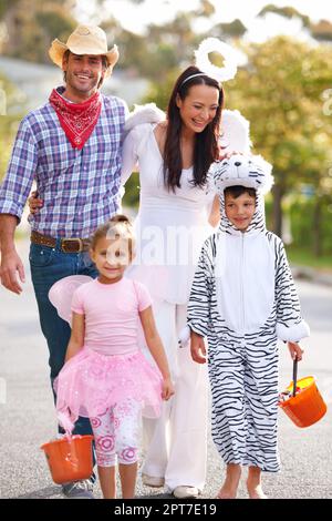 Es ist ein toller Abend für ein paar Süßes oder Saures. Eine Familie, die die Straße entlang läuft, in ihren Halloween-Kostümen Stockfoto