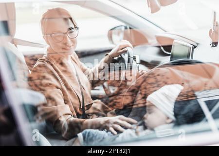 Mutter konzentriert sich darauf, mit dem Familienauto Besorgungen zu machen, während ihr Baby auf dem Kindersitz neben ihrem Standort schläft Stockfoto