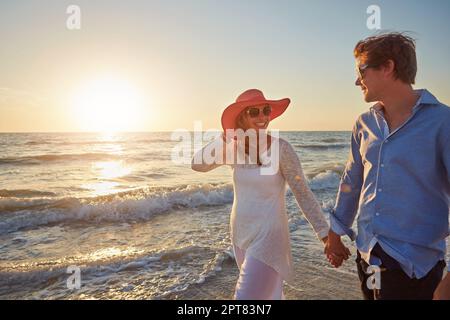 Nichts sagt Romantik besser aus als ein Spaziergang bei Sonnenuntergang am Strand. Ein glückliches Paar, das am Strand spaziert. Stockfoto