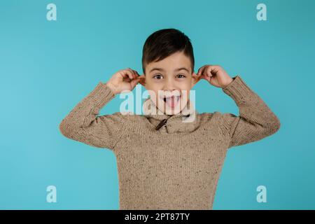 Fröhlicher lustiger kleiner Junge, der ihre Zunge auf blauem Hintergrund zeigt. Gesichtsausdruck Stockfoto