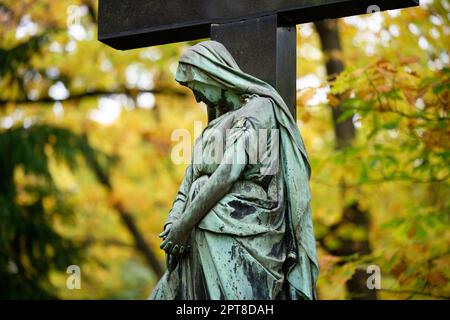 Trauernde Frauenskulptur vor einem Kreuz auf einem Herbstfriedhof Stockfoto