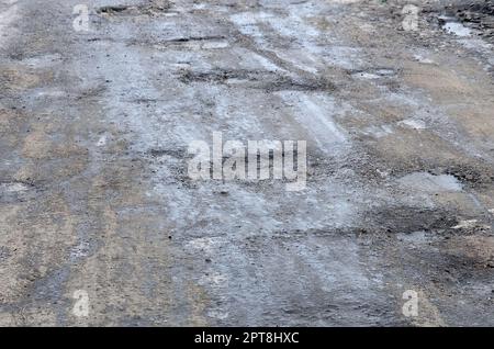 Beschädigte Asphaltstraße mit Schlaglöchern durch Gefrier- und Auftauzyklen im Winter. Schlechte Straße Stockfoto