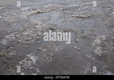 Beschädigte Asphaltstraße mit Schlaglöchern durch Gefrier- und Auftauzyklen im Winter. Schlechte Straße Stockfoto