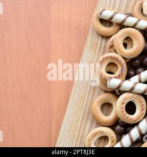 Knusprige Tuben, Schokoladenschmelzkugeln und Bagels liegen auf einer Holzfläche. Mischung aus verschiedenen Süßigkeiten Stockfoto