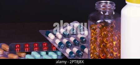 Pillen und Tabletten in verschiedenen Farben sind gestreut und in Flaschen auf dunklem Hintergrund Stockfoto