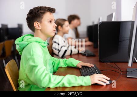 Konzentriert zwischen Jungen, die mit Klassenkameraden im Computerlabor studieren Stockfoto