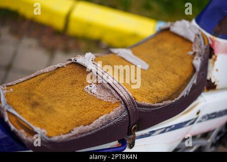 Brauner Motorrad-Sattelbezug aus Kunstleder (PVC oder PU), gerissen, um den Schwamm im Inneren zu sehen. Stockfoto