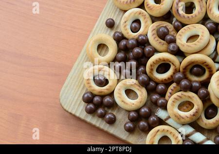 Knusprige Tuben, Schokoladenschmelzkugeln und Bagels liegen auf einer Holzfläche. Mischung aus verschiedenen Süßigkeiten Stockfoto