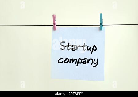 Startup-Unternehmen. Die Notiz ist auf einem weißen Aufkleber geschrieben, der mit einer Wäscheklammer an einem Seil auf einem beigen Hintergrund hängt Stockfoto