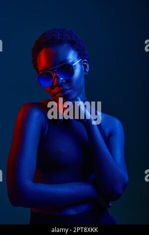 Nachdenkliche Frau in Sonnenbrille mit dunklem Studiohintergrund, Kopierbereich und Neonlicht Stockfoto