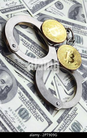 Polizei Handschellen und Bitcoins liegen auf eine große Anzahl von Dollarnoten. Das Konzept der Probleme mit dem Gesetz während der Illegalen cryptocurrency Bergbau- und Stockfoto