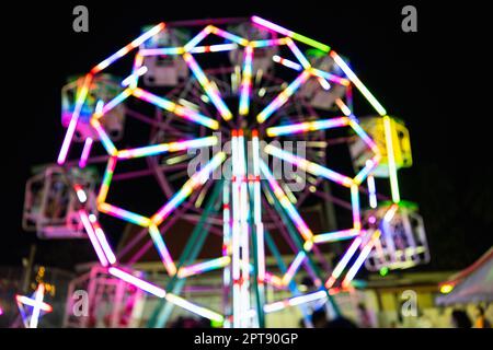 Verschwommene Achterbahn in Bokeh, Riesenrad in der Nacht von bunten mit Outdoor, unscharf (verschwommen) und verschwommen Bild des Vergnügungsparks, der jährliche Tempel Stockfoto