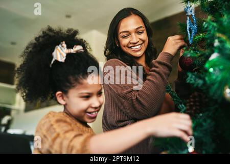 Nur Mami und ich schneiden den Baum. Eine glückliche junge Mutter und Tochter, die zu Hause den Weihnachtsbaum schmücken Stockfoto