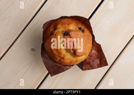 Blick von oben auf frischen Muffin mit Schokoladenstückchen in Papierverpackung auf einem Holztisch Stockfoto