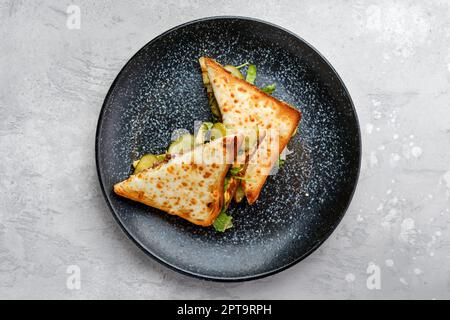 Draufsicht auf Sandwich mit Rindfleisch, eingelegter Gurke und Käse auf Dreiecksstücken Stockfoto