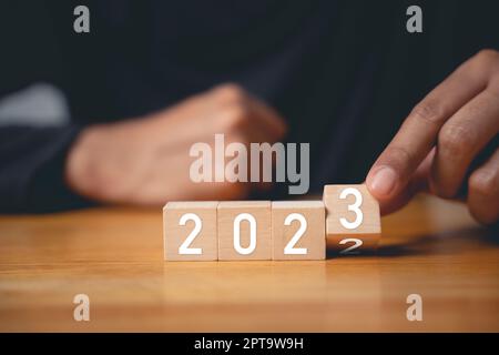 Frohes Neues Jahr 2023. Geschäftsmann dreht Holzwürfel Nr. 2 zu Nr. 3 für Neujahr 2023 um und setzt Zielplan für Geschäftsziel „Start Success Business“ Stockfoto