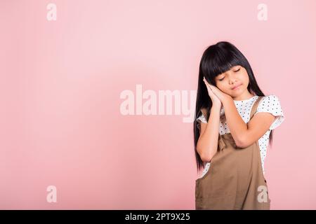 Asiatisches kleines Kind 10 Jahre alt stehend mit verschlossenen Händen, so als ob er schläft, geschlossene Augen im Studio, isoliert auf rosa Hintergrund, Happy Child Stockfoto