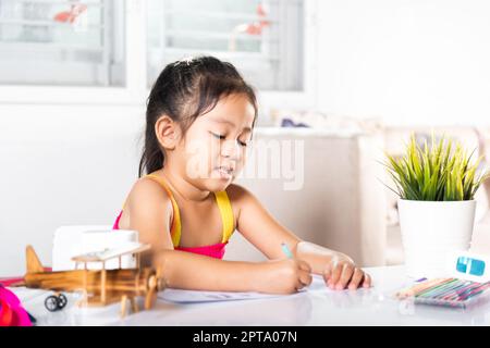 Kind kleines Mädchen Zeichentrickfilm auf Papier vor malen die Farbe, asiatische niedliche Kind Vorschulkinder sitzen auf dem Tisch lächelnd sie zeichnen und schreiben ein Bild Stockfoto