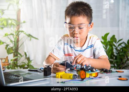 Asiatischer Junge stecken Energie-und Signalkabel an Sensor-Chip mit Arduino Roboterauto, kleines Kind aus der Ferne lernen online mit Auto-Spielzeug, DAMPF Bildung Stockfoto