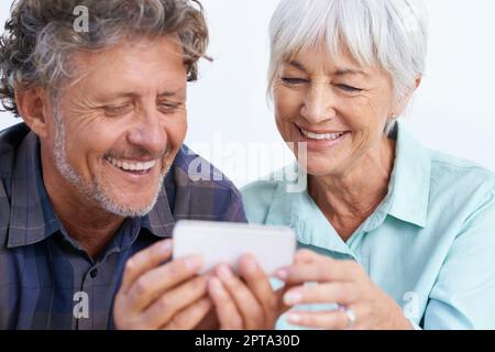 So viele gute zur Auswahl. Ein glückliches Seniorenpaar, das zusammen auf einen Handybildschirm schaut Stockfoto