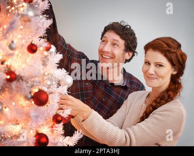 Der Baum bekommt den letzten Schliff. Porträt eines liebevollen Paares, das einen weißen Weihnachtsbaum schmückt Stockfoto