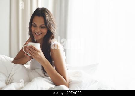 Sie beginnt ihren Tag mit Koffein. Eine schöne junge Frau, die eine Tasse Kaffee im Bett genießt Stockfoto