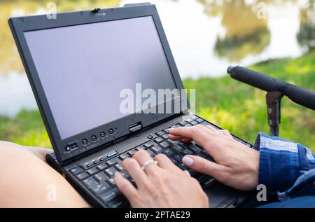 Das Mädchen sitzt auf einem Stuhl in der Nähe des Herbstsees und arbeitet auf einem Laptop freiberuflicher Camping. Roboter aus dem Büro, telefonierte mit Kollegen Stockfoto