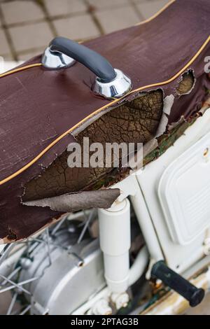 Brauner Motorrad-Sattelbezug aus Kunstleder (PVC oder PU), gerissen, um den Schwamm im Inneren zu sehen. Stockfoto