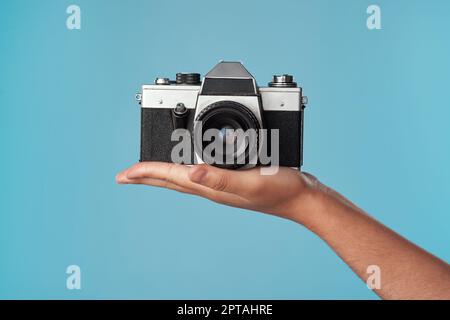 Die beste Kamera in der Fotobranche. Studiofoto einer unbekannten Frau, die eine Kamera vor blauem Hintergrund hält Stockfoto