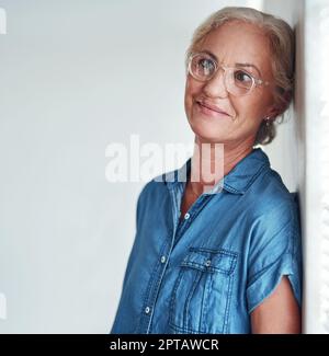 Shes hatte viel im Kopf. Eine attraktive ältere Frau, die sich an einer Wand lehnte und besinnlich aussagt, während sie vor einem grauen Hintergrund posierte Stockfoto