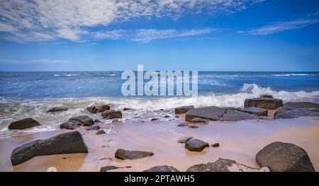 Rocky Beach in Alexandra Headland, Maroochydore, Sunshine Coast, Queensland. Die Flut kommt, Sand ist nass und Brandungswellen brechen über die Felsen Stockfoto