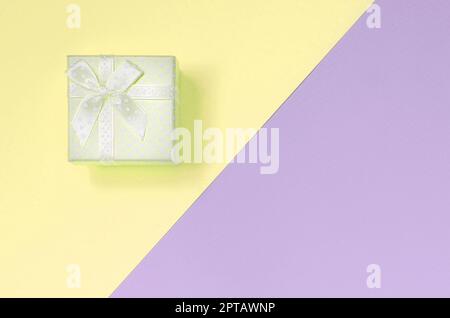 Kleiner gelber Geschenkbox liegen auf Textur Hintergrund der Mode pastell Gelb und Violett Farben Papier in minimalen Begriff. Stockfoto