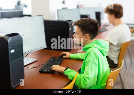 Konzentriert zwischen Jungen, die mit Klassenkameraden im Computerlabor studieren Stockfoto