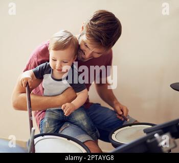 Listen....ca, du hörst es. Ein attraktiver junger Vater, der seinem Sohn das Trommeln beibringt Stockfoto