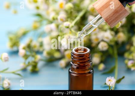 Ätherisches Öl in die Glasflasche auf dem hellblauen Tisch tropfen lassen, Nahaufnahme. Platz für Text Stockfoto