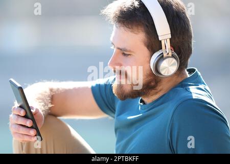 Mann mit Kopfhörern, der Musik hört und Inhalte von Smartphones ansieht Stockfoto