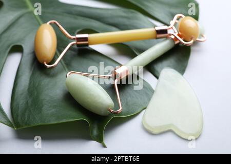 Gua-sha-Stein, verschiedene Gesichtsrollen und Monstera-Blatt auf hellem Hintergrund Stockfoto