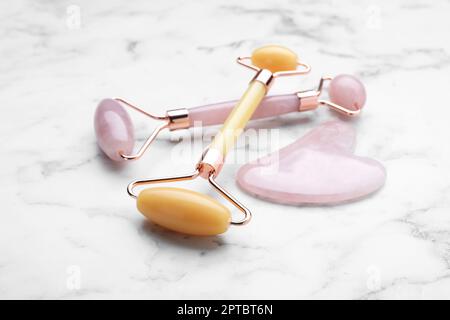 Gua-Sha-Stein und verschiedene Gesichtsrollen auf einem weißen Marmortisch Stockfoto