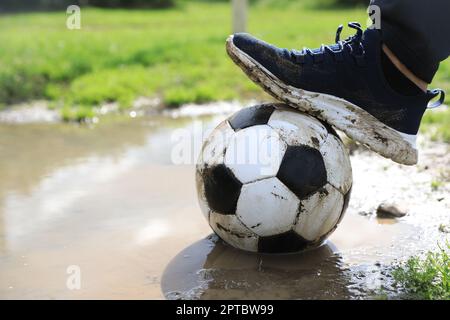 Mann mit schmutzigem Fußball in der Nähe der Pfütze draußen, Nahaufnahme Stockfoto