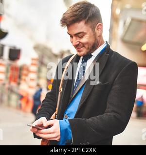 Mein Telefon funktioniert heute härter als ich. Ein junger, gut gekleideter Mann schreibt auf sein Handy, während er auf ein Taxi wartet, um ihn morgens zur Arbeit zu bringen Stockfoto