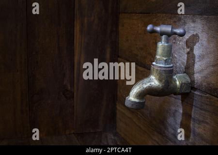 Ein alter Messinghahn an einer rustikalen Holzwand in sanfter, dunkler Stimmungsbeleuchtung mit Kopierbereich links vom Rahmen Stockfoto