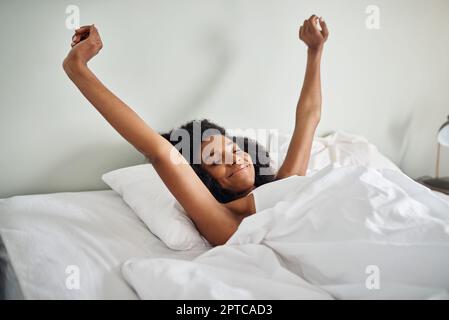 Ich fühle mich gut ausgeruht. Eine attraktive junge Frau, die sich im Bett streckt Stockfoto