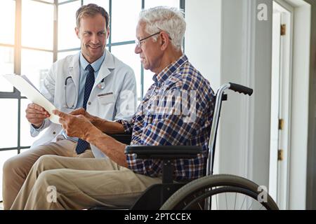 Dann gehen wir es gemeinsam durch. Ein männlicher Arzt, der mit einem Seniorenpatienten im Altersheim spricht. Stockfoto