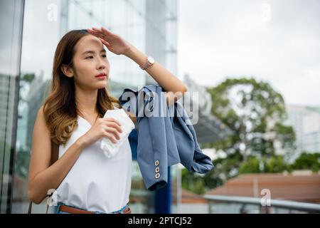 Wütend weiblich mit Sonnenstich Hautschäden von Sonne UV-Stadt Luftverschmutzung draußen auf der Straße, Überhitzung asiatische schöne Geschäftsfrau trocknet Schweiß er Stockfoto