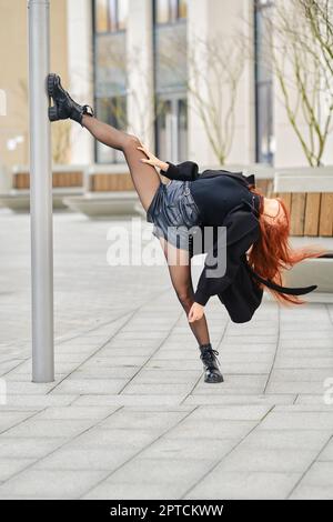 Die flexible junge Frau zeigt sich gespalten, indem sie ihren Fuß auf einen Stock setzt Stockfoto