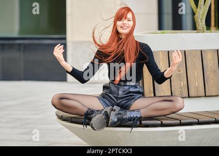 Rothaarige, lustig lachende junge Frau, die auf einer Bank sitzt Stockfoto