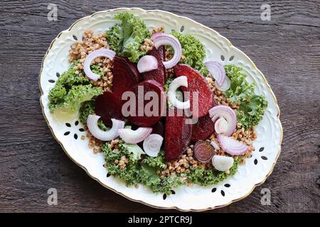 Warmer Buchweizen- und Rote-Bete-Salat auf Holzhintergrund. Vegetarische Diätidee und Rezept - Salat mit Rote Bete, Buchweizen, Grünkohl, Zwiebeln, frischen Kräutern. Oben Stockfoto